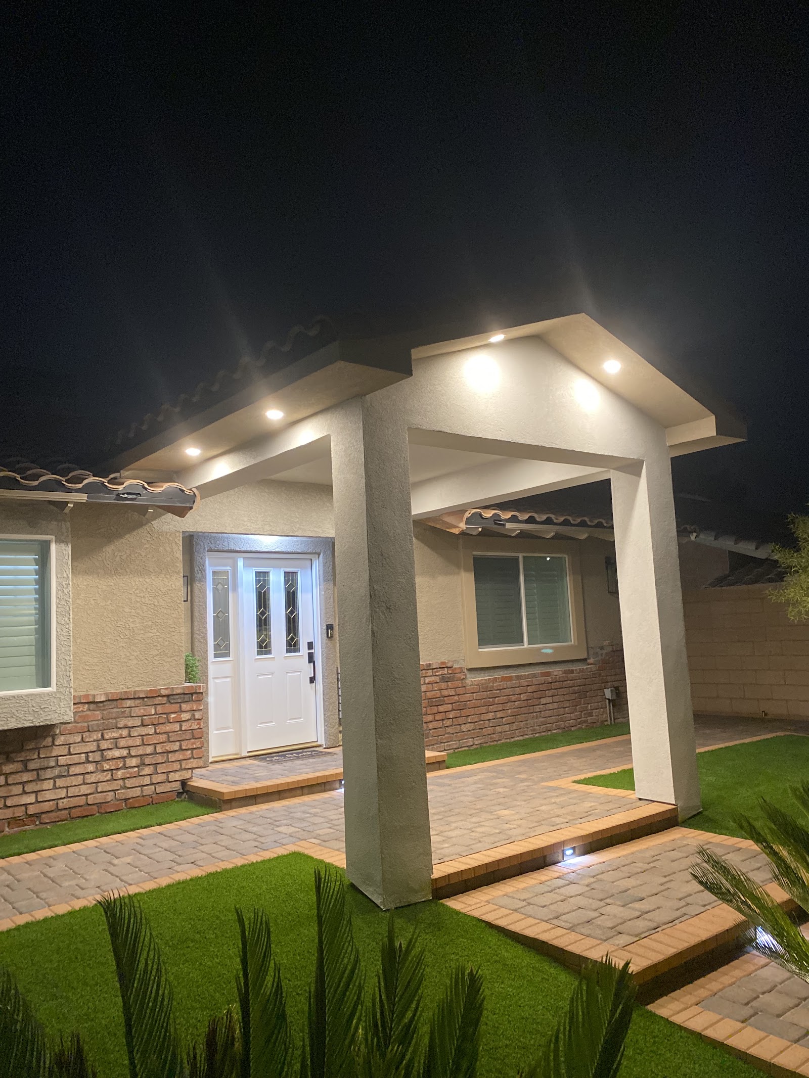 Finished front entry porch at night with recessed lighting, pavers and artificial turf